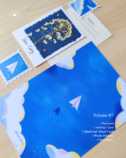 Postcard with a paper plane flying illustrations, washi sticker in a stamp shape with paper plane and cloud illustrations, handcrafts dry pressed flower on a blue recycle paper